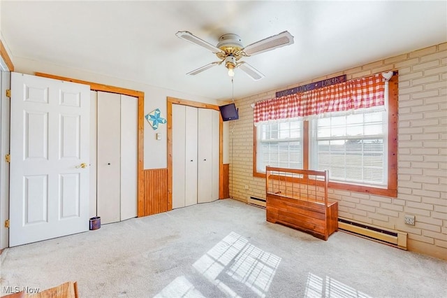 bedroom featuring multiple closets, ceiling fan, baseboard heating, light colored carpet, and brick wall