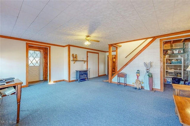 interior space with carpet floors, a wood stove, ceiling fan, and crown molding