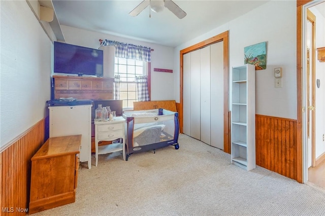 bedroom with light carpet, a closet, ceiling fan, and wood walls