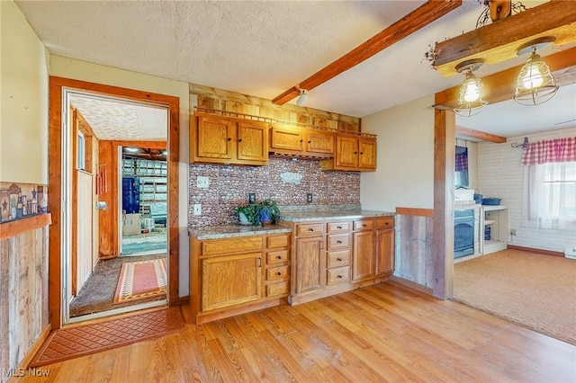 kitchen with a textured ceiling, a fireplace, light hardwood / wood-style floors, and beamed ceiling