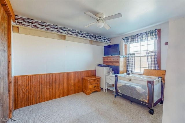 carpeted bedroom featuring ceiling fan and wood walls