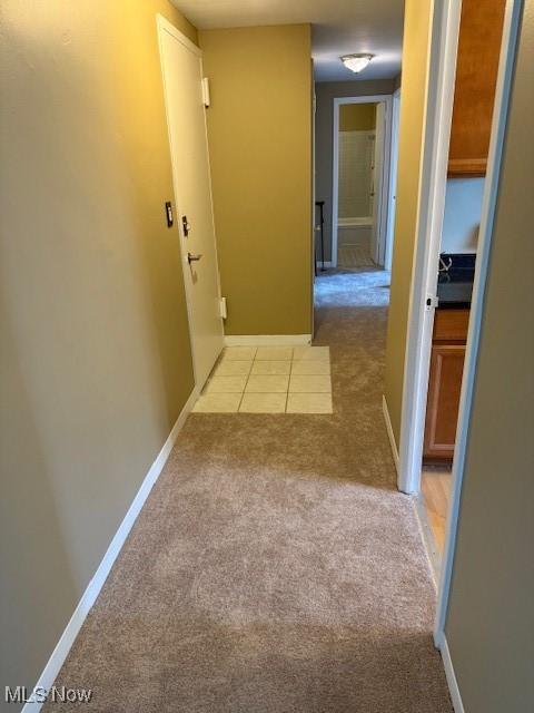 hall with light tile patterned flooring, baseboards, and light colored carpet