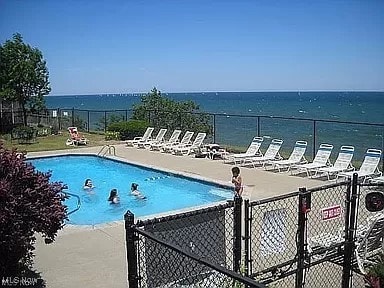 community pool featuring a water view, fence, and a gate