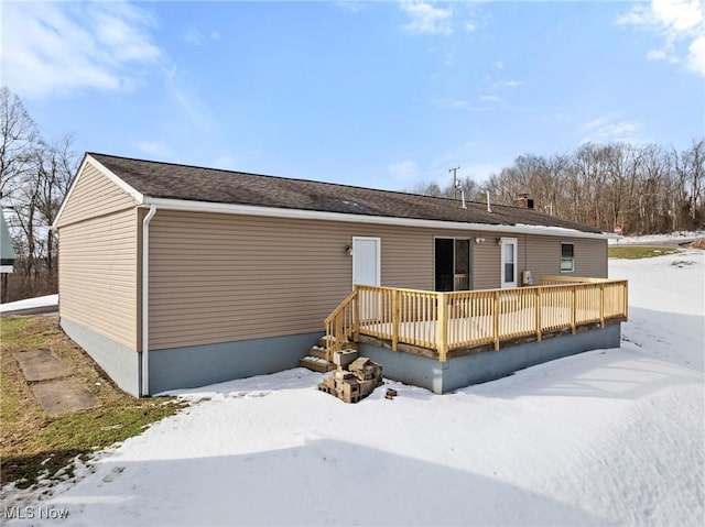 snow covered back of property with a wooden deck