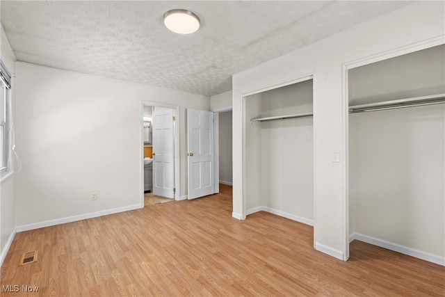 unfurnished bedroom with multiple closets, ensuite bath, a textured ceiling, and light wood-type flooring