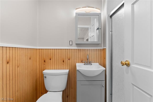 bathroom with vanity, toilet, and wood walls