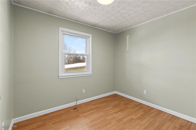 empty room featuring crown molding, light hardwood / wood-style floors, and a textured ceiling