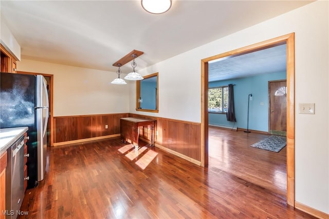 kitchen with stainless steel appliances, dark wood-type flooring, pendant lighting, and wood walls