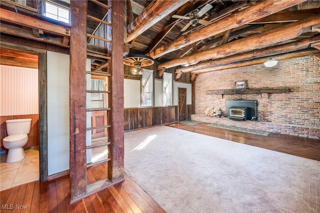 unfurnished living room featuring beamed ceiling, a wood stove, hardwood / wood-style floors, and high vaulted ceiling