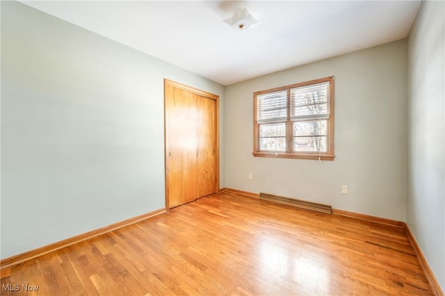 unfurnished bedroom with a baseboard radiator, light wood-type flooring, and a closet