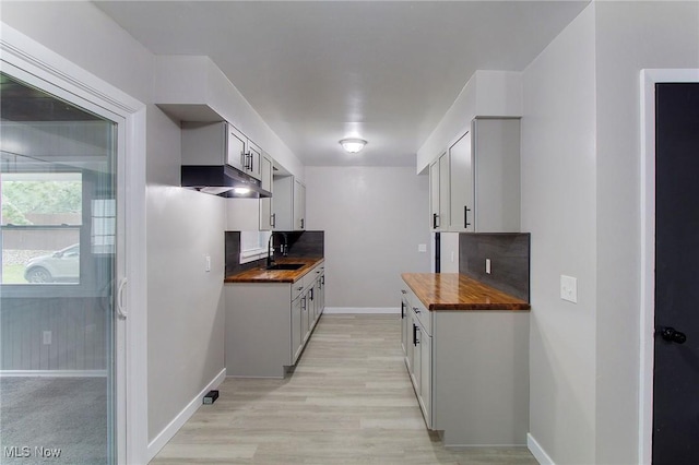 kitchen with butcher block counters, extractor fan, sink, light hardwood / wood-style flooring, and decorative backsplash