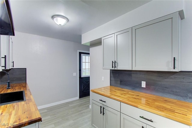 kitchen featuring tasteful backsplash, sink, butcher block countertops, and light hardwood / wood-style flooring