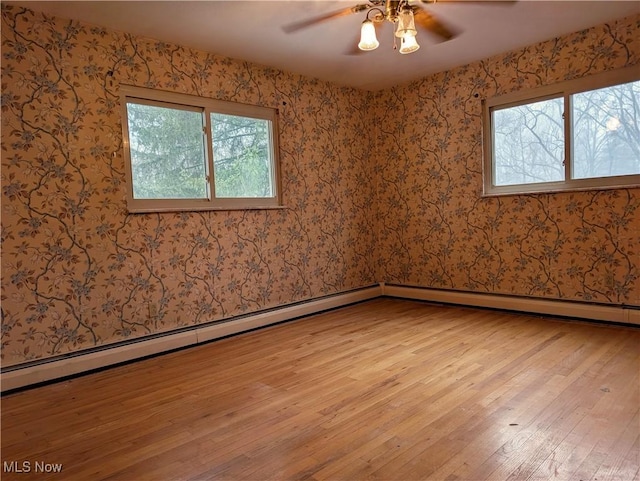 unfurnished room with a baseboard heating unit, ceiling fan, a healthy amount of sunlight, and light wood-type flooring