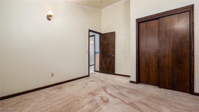 unfurnished bedroom featuring ornamental molding, a towering ceiling, light carpet, and a closet