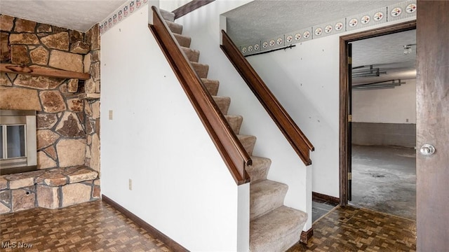 stairs featuring a fireplace, parquet flooring, and a textured ceiling