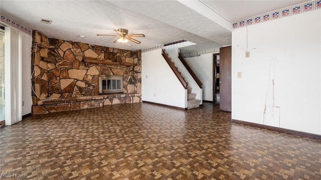 unfurnished living room with ceiling fan, dark parquet floors, a stone fireplace, and a textured ceiling