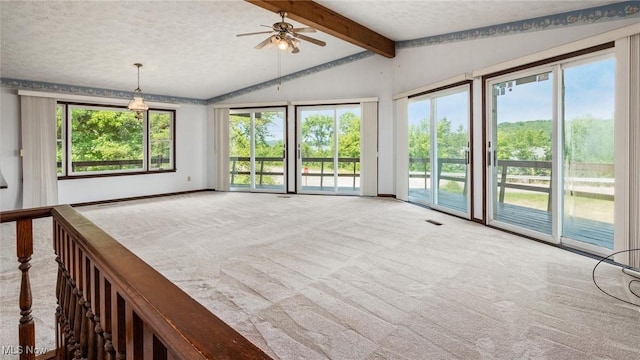 unfurnished living room with a wealth of natural light, lofted ceiling with beams, a textured ceiling, and carpet