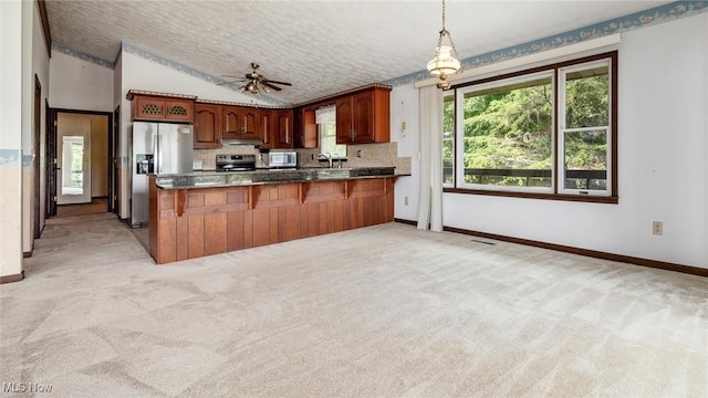 kitchen with sink, decorative light fixtures, kitchen peninsula, light colored carpet, and stainless steel appliances