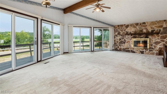 unfurnished living room with lofted ceiling with beams, ceiling fan, a stone fireplace, and carpet floors