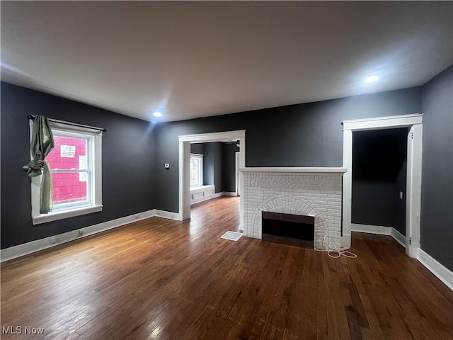 unfurnished living room featuring hardwood / wood-style flooring and a brick fireplace