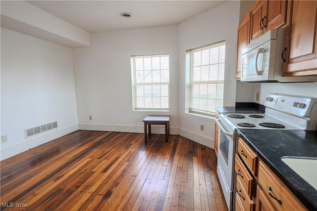 kitchen featuring dark wood-type flooring, white appliances, and dark stone counters