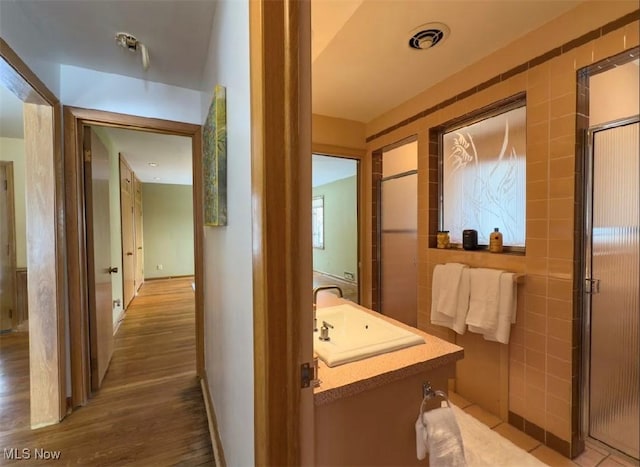 bathroom featuring vanity, hardwood / wood-style floors, a shower with shower door, and tile walls