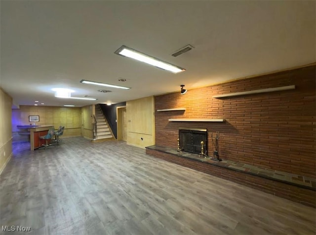 basement with brick wall, wood-type flooring, and a brick fireplace