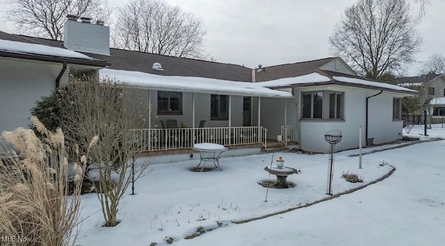 snow covered back of property with covered porch