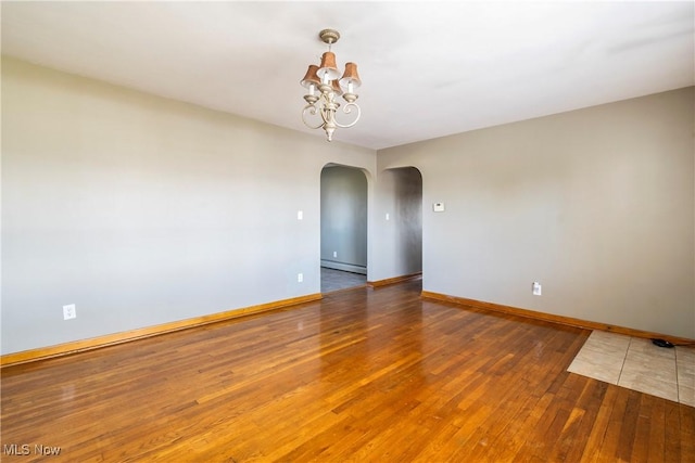 spare room featuring an inviting chandelier, dark wood-type flooring, and a baseboard radiator