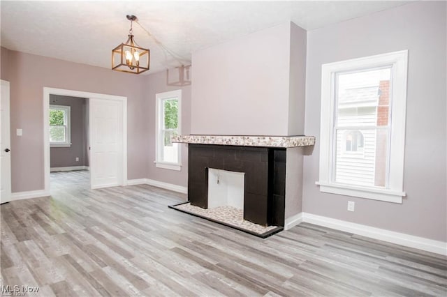 unfurnished living room featuring light wood-type flooring, a fireplace, an inviting chandelier, and plenty of natural light