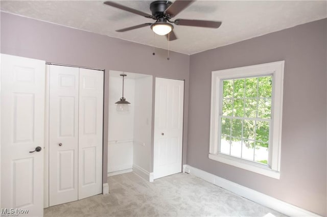 unfurnished bedroom featuring ceiling fan, light colored carpet, and two closets