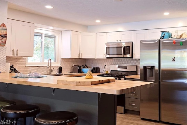 kitchen featuring white cabinetry, appliances with stainless steel finishes, a kitchen bar, and butcher block counters