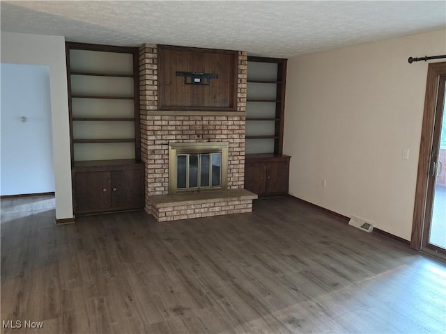 unfurnished living room featuring dark wood-type flooring, built in features, a fireplace, and a textured ceiling