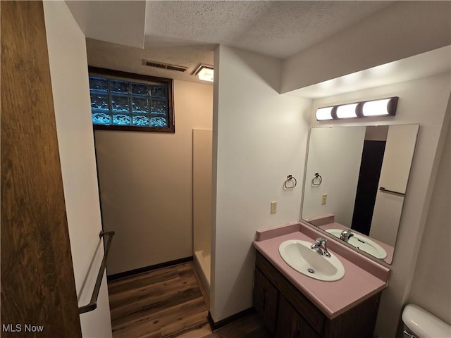 bathroom with vanity, wood-type flooring, a textured ceiling, toilet, and walk in shower