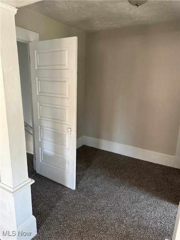 unfurnished room with a textured ceiling and dark colored carpet