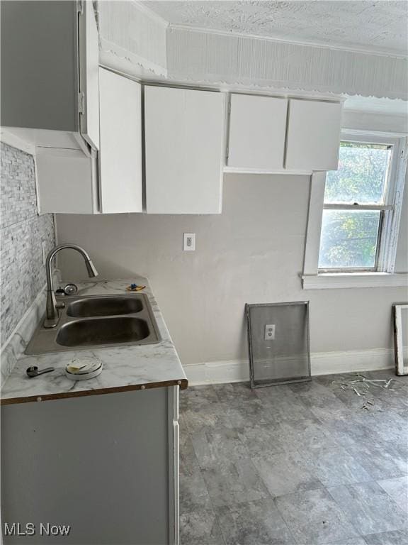 kitchen with white cabinetry, sink, crown molding, and a textured ceiling