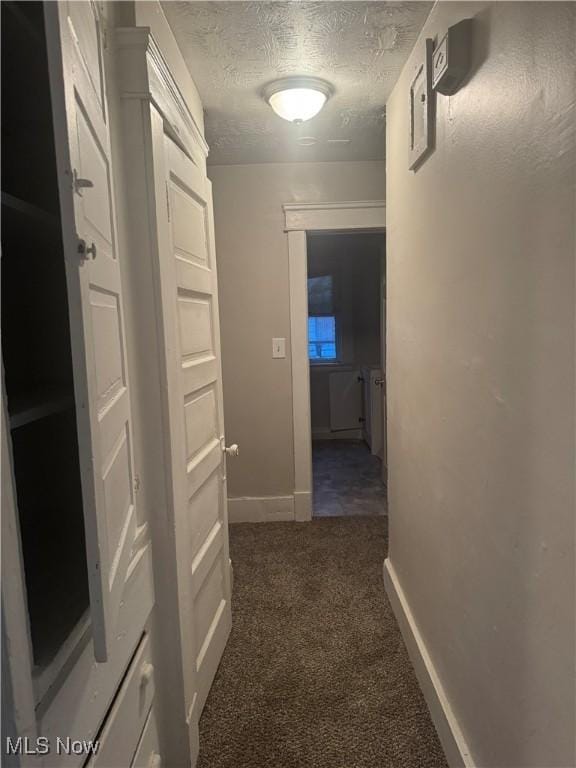 hallway featuring a textured ceiling and dark colored carpet