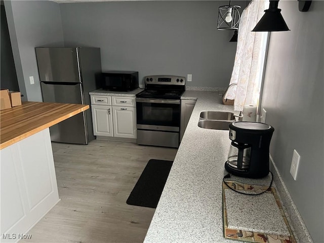 kitchen with butcher block countertops, hanging light fixtures, stainless steel appliances, white cabinets, and light wood-type flooring