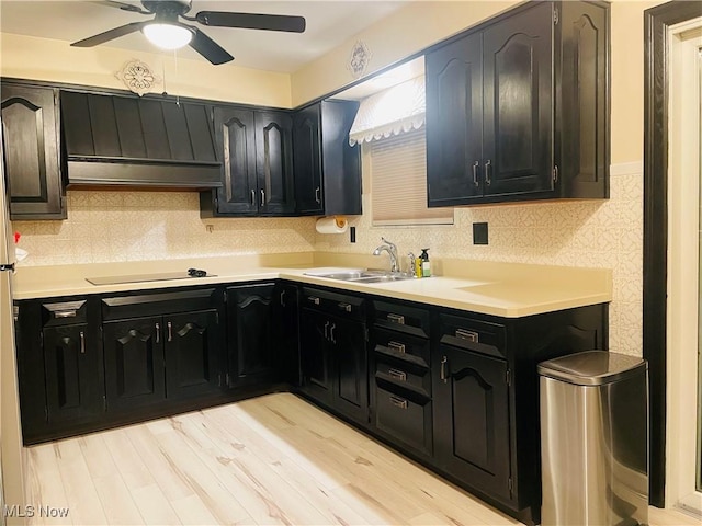 kitchen featuring a sink, black electric cooktop, light countertops, under cabinet range hood, and backsplash