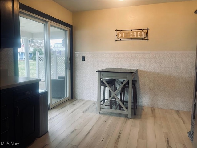 doorway with light wood-style floors, a wainscoted wall, and tile walls