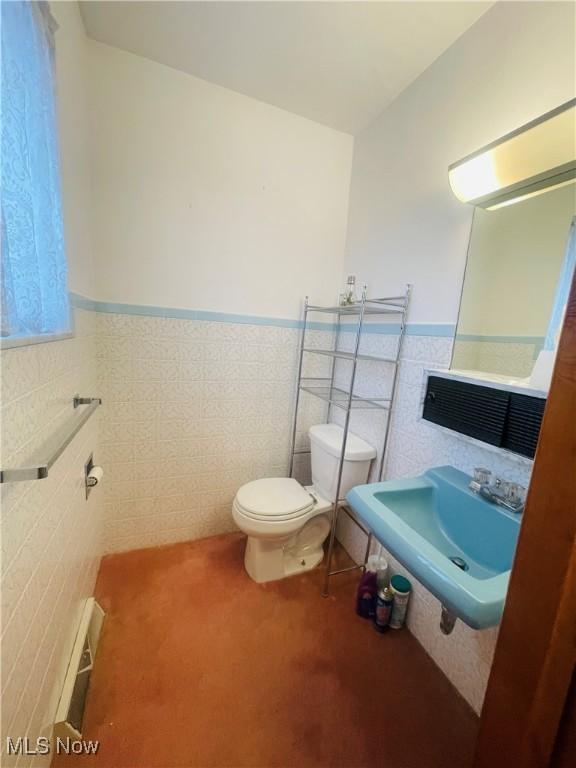 half bath with tile walls, visible vents, toilet, wainscoting, and a sink