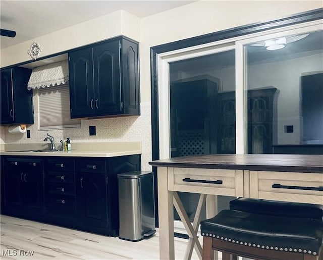 kitchen with light countertops, backsplash, light wood-style floors, a sink, and dark cabinetry