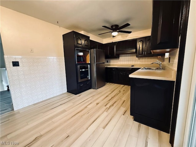 kitchen featuring under cabinet range hood, stainless steel appliances, a sink, light wood-style floors, and light countertops