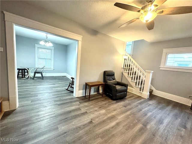 living area featuring dark wood-type flooring, ceiling fan with notable chandelier, and a textured ceiling