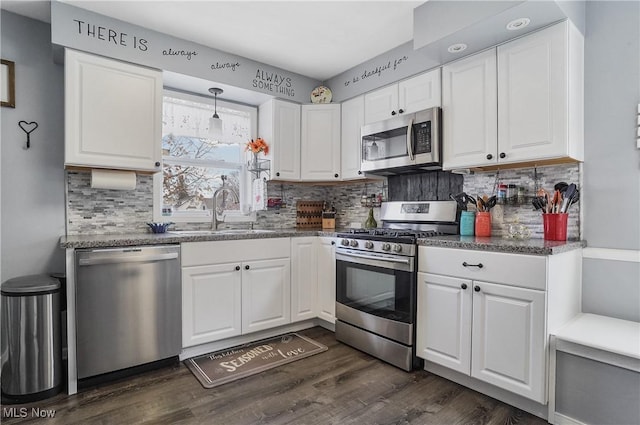 kitchen featuring appliances with stainless steel finishes, pendant lighting, sink, white cabinets, and dark hardwood / wood-style flooring