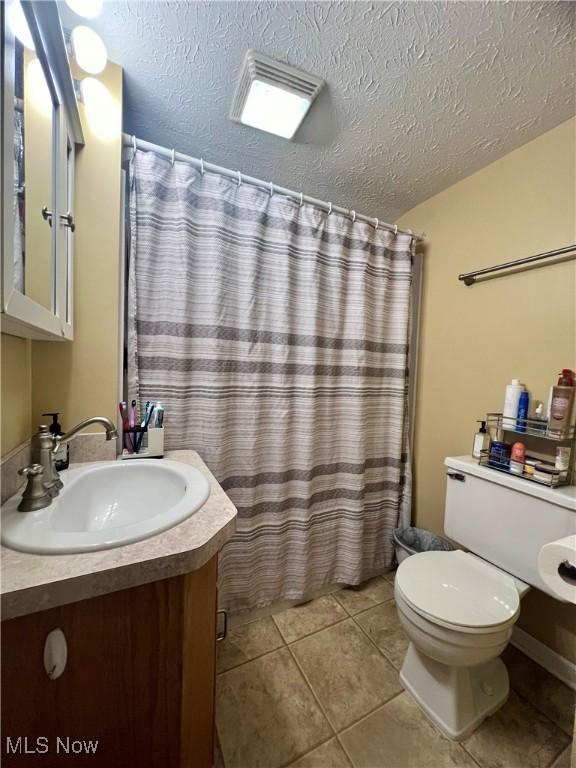 bathroom with tile patterned flooring, vanity, a textured ceiling, and toilet