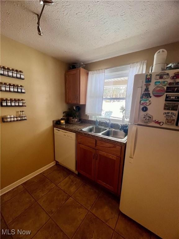 kitchen with white appliances, sink, a textured ceiling, and dark tile patterned floors