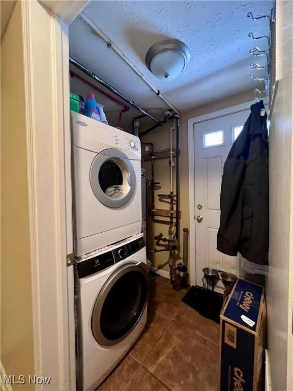 washroom with stacked washer / dryer, dark tile patterned flooring, and a textured ceiling