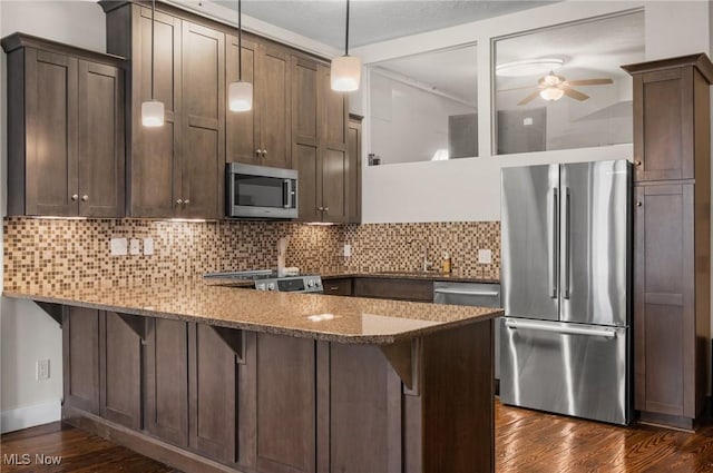 kitchen with appliances with stainless steel finishes, decorative light fixtures, kitchen peninsula, and stone counters