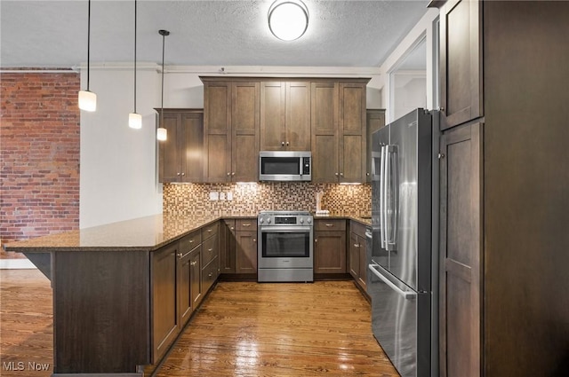 kitchen with pendant lighting, stainless steel appliances, a kitchen bar, kitchen peninsula, and dark stone counters